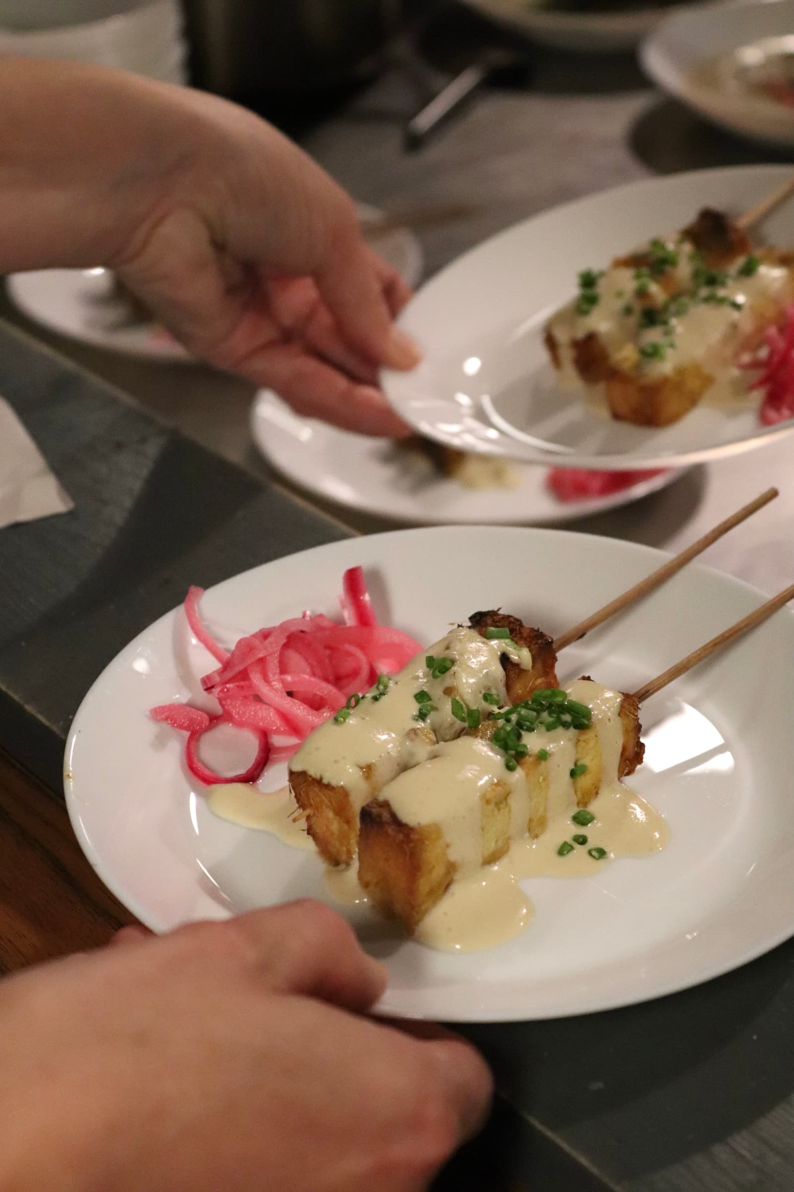A hand serving white plate full of colourful food