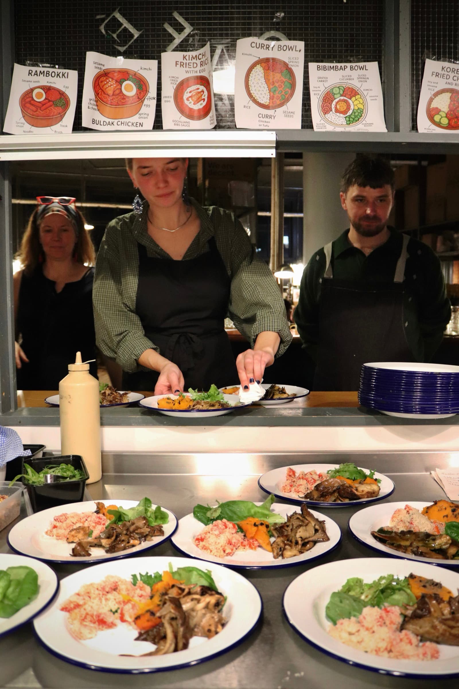 Chefs plating dishes beneath illustrated menu cards